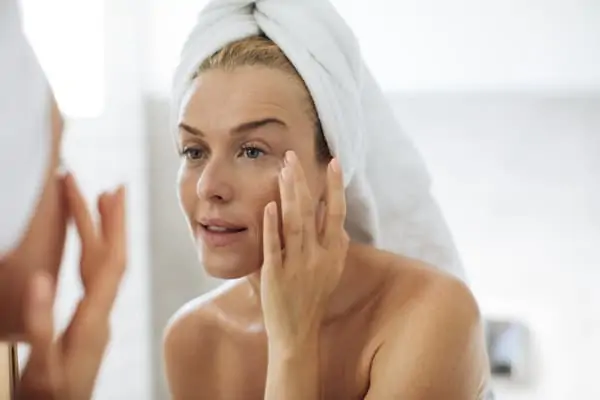 Beautiful Caucasian woman in towels looking her face in mirror and putting creme on.