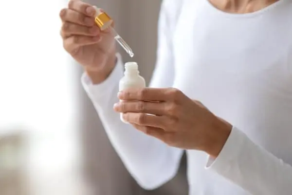 Close up young woman holding bottle with pipette, using face serum.