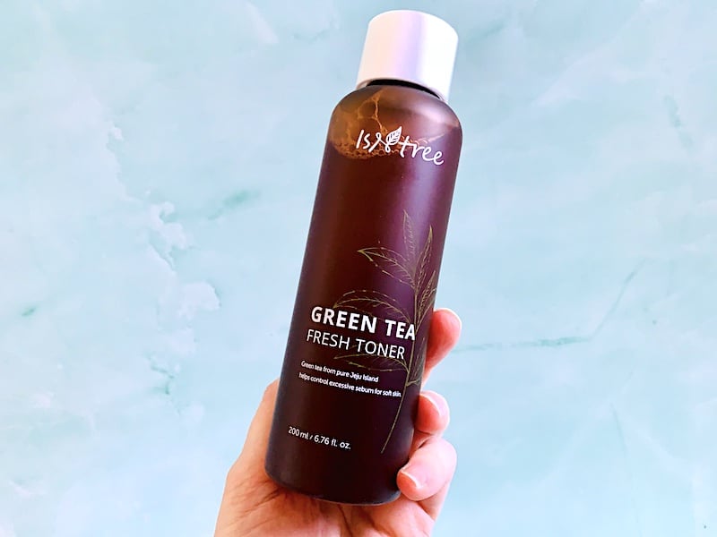 Isntree Green Tea Fresh Toner held by hand on green background