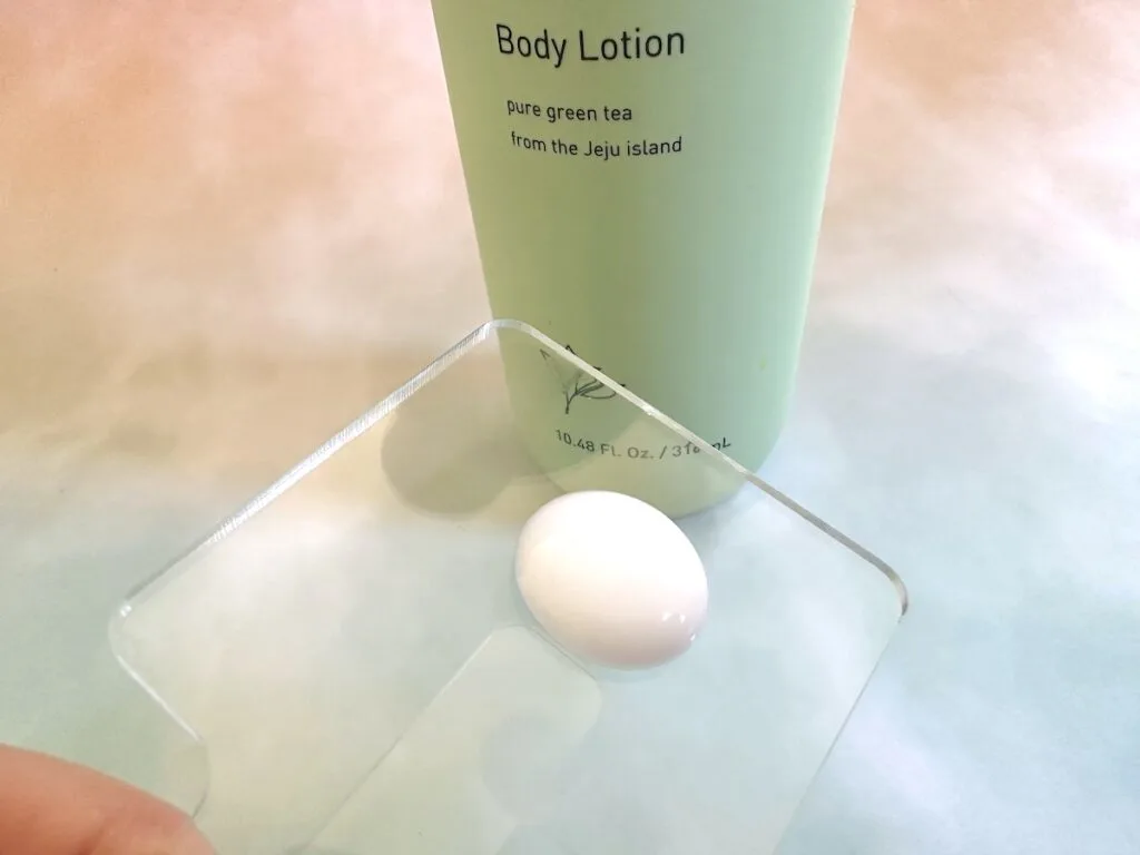 innisfree Green Tea Pure Body Lotion bottle behind behind lotion sample on clear spatula.