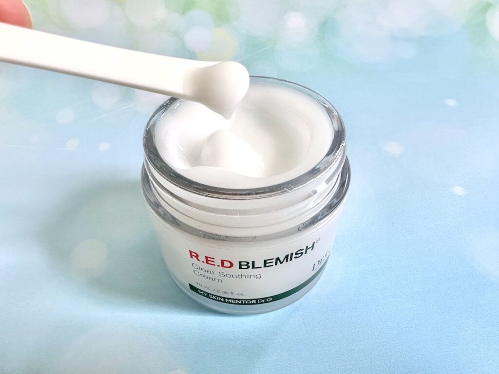 Dr.G R.E.D Blemish Clear Soothing Cream, open jar with moisturizer sample on white cosmetic spatula.
